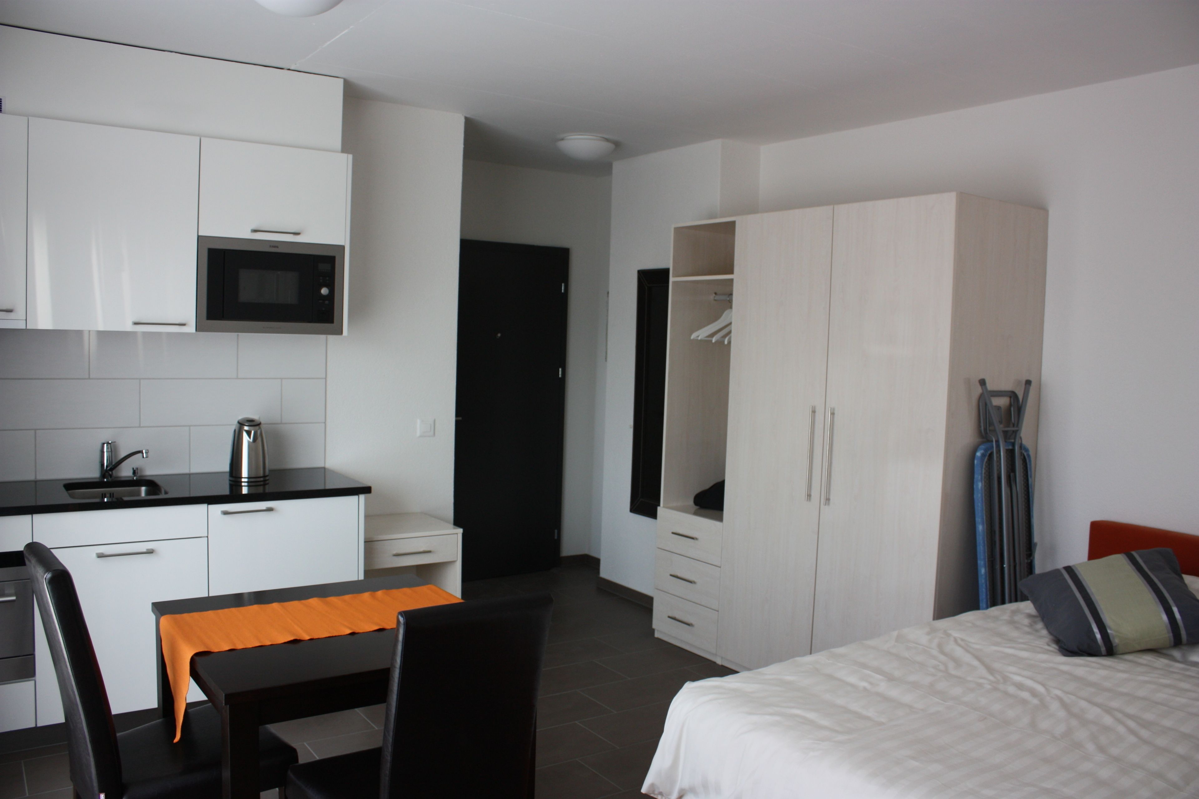 Una habitación de hotel con cama, escritorio, silla, kitchenette y armario.
