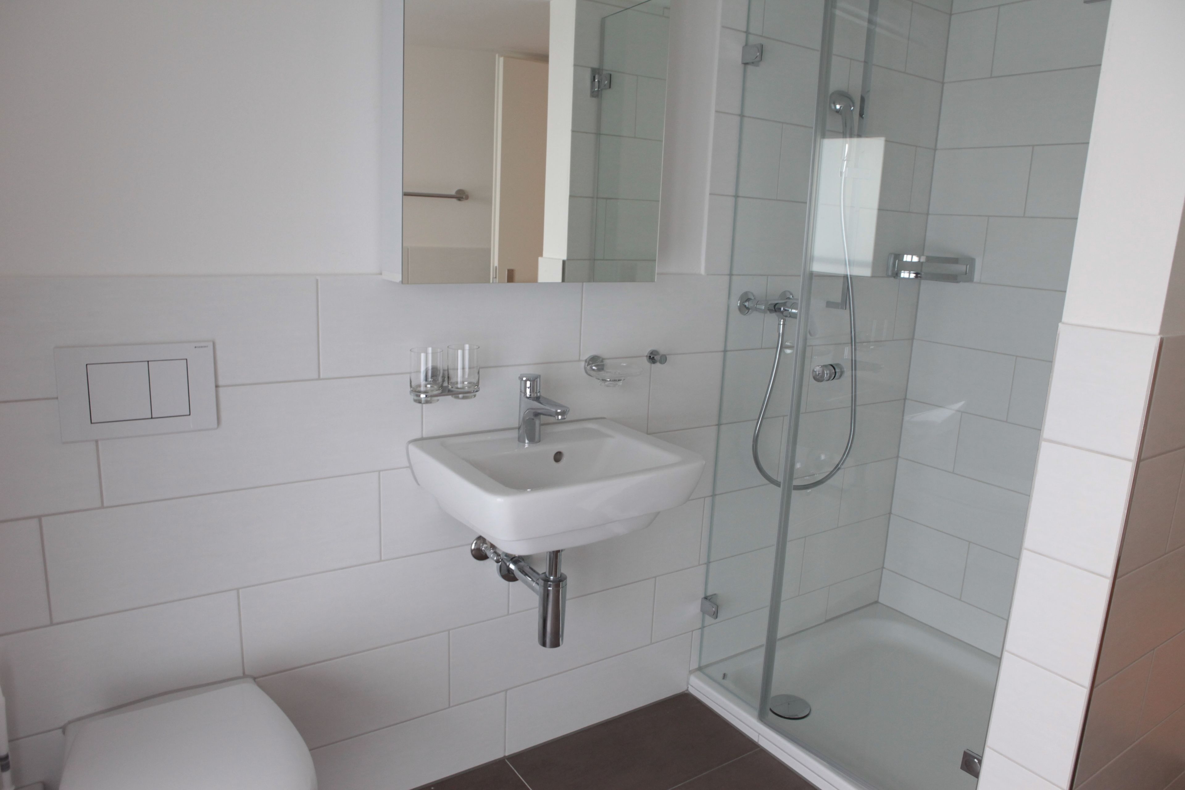 Un baño moderno con lavamanos blanco, espejo y cabina de ducha con mampara de vidrio.