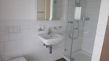 Un baño moderno con lavamanos blanco, espejo y cabina de ducha con mampara de vidrio.