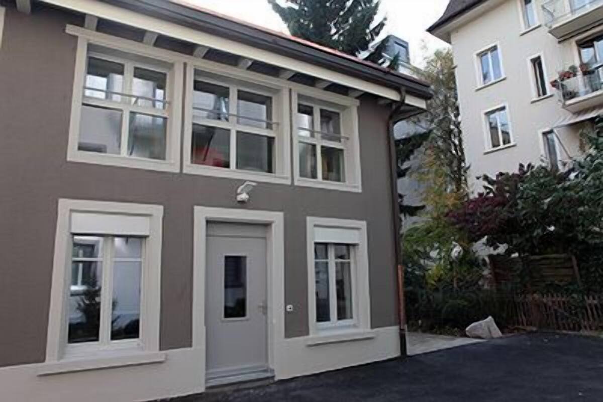 A two-story residential building with a grey facade, white-framed windows, and a small front door.