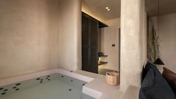 A spa area with a large bathtub, a wicker basket, and a dark-colored bench.
