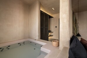 A spa area with a large bathtub, a wicker basket, and a dark-colored bench. - Emery Suites (Naxos)