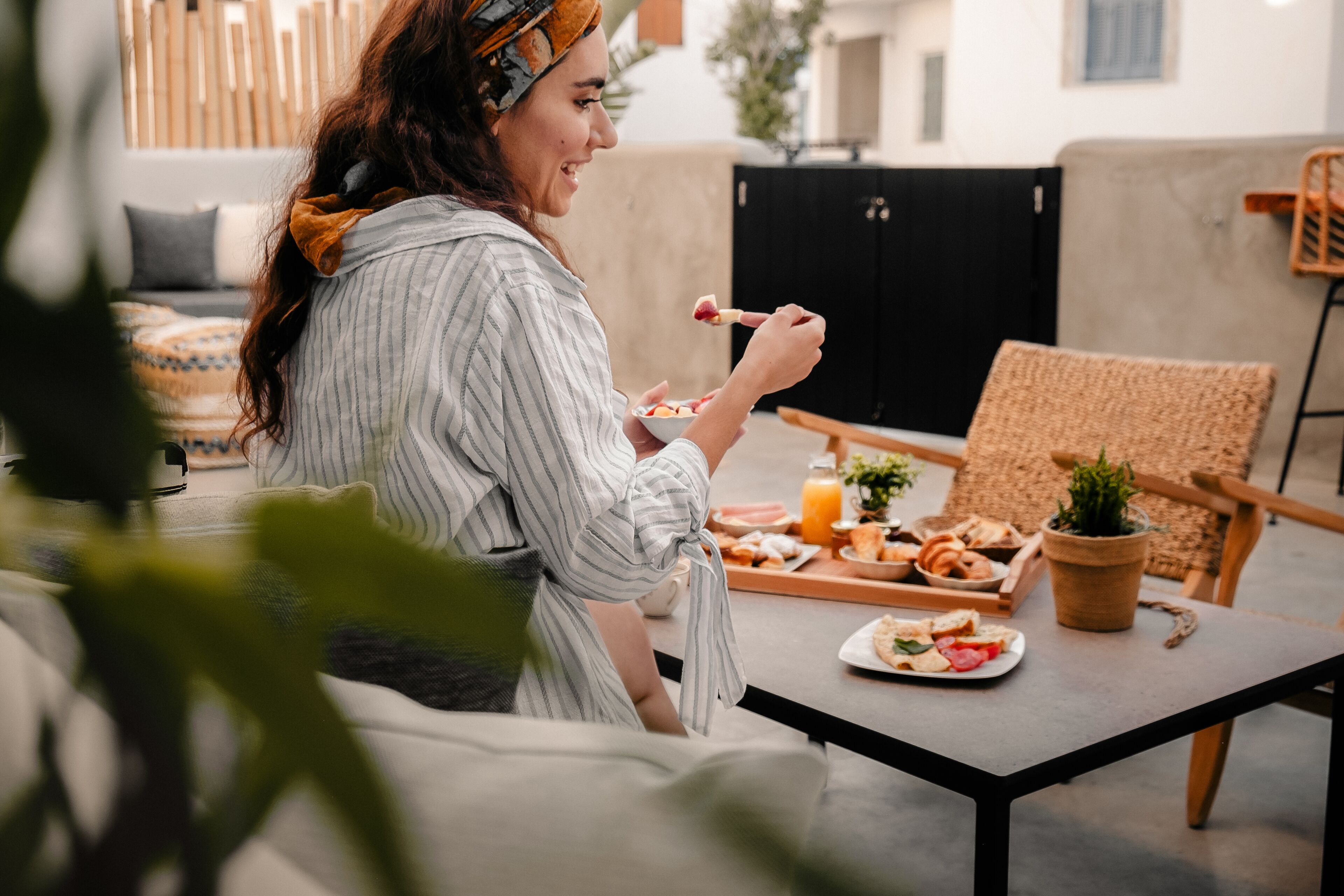 A person sitting at an outdoor table with a meal, a sofa, and a potted plant in the background.