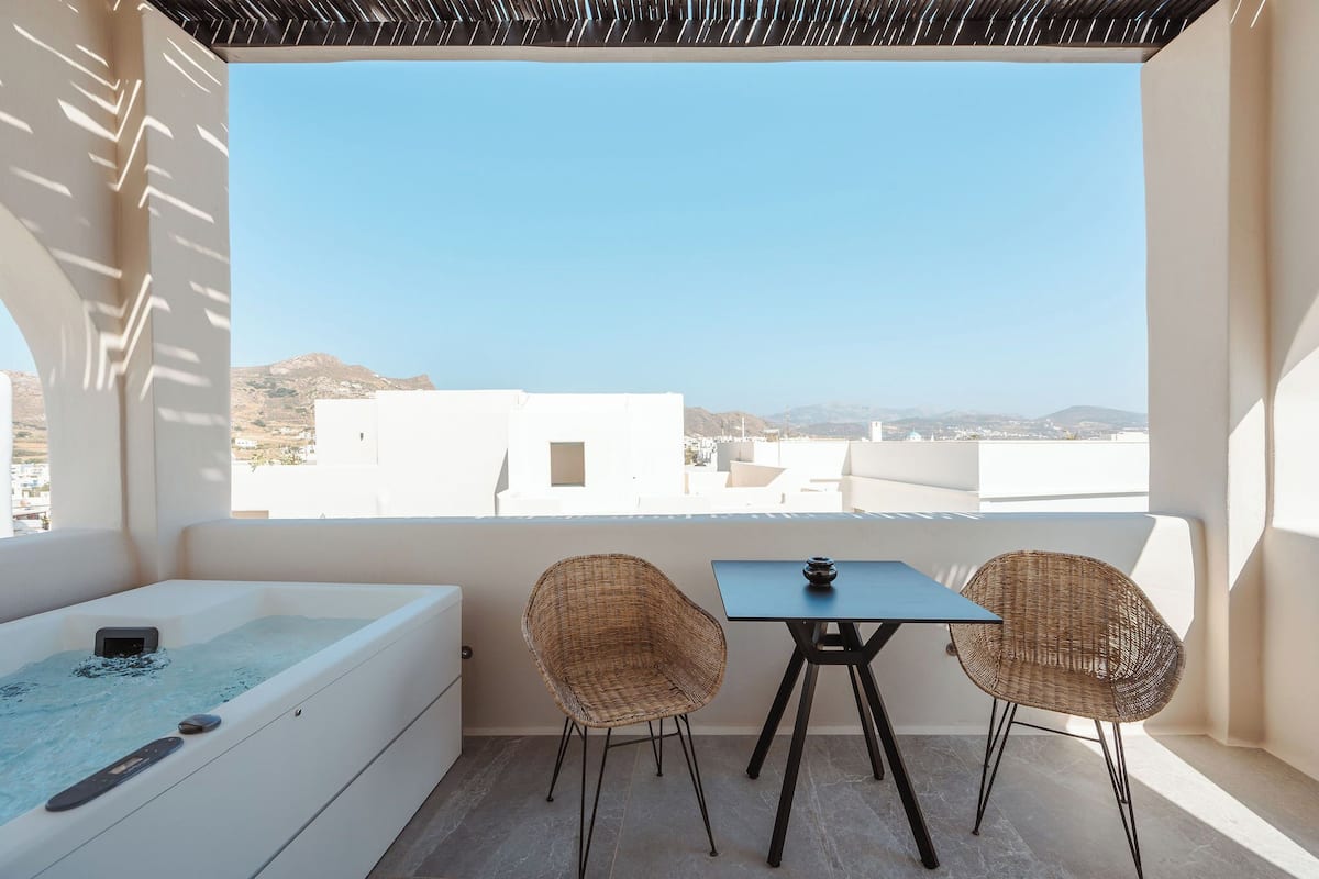 Un balcón con jacuzzi, dos sillones de mimbre y una mesa.
