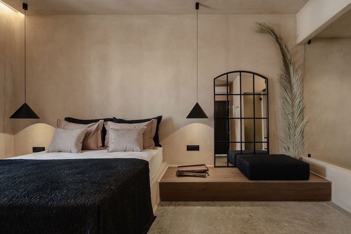 Un dormitorio moderno con cama, lámparas de noche, un pequeño banco y una planta alta.