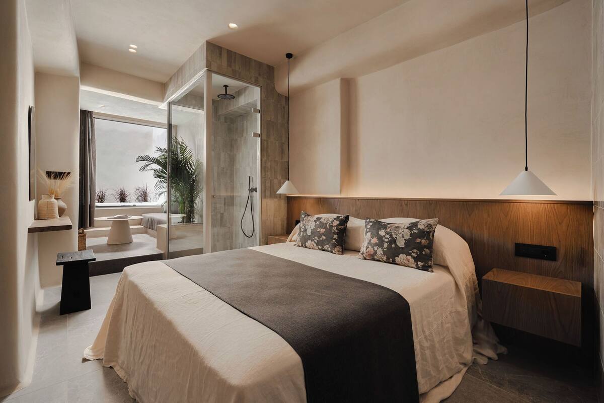 Un dormitorio moderno con una cama grande, una mesita de noche, una cabecera y un box de ducha de vidrio, además de vistas al exterior.