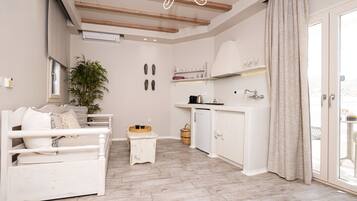 Una sala de estar moderna con un sofá blanco, una mesita, una planta y una zona de cocina con un armario blanco y un lavamanos.