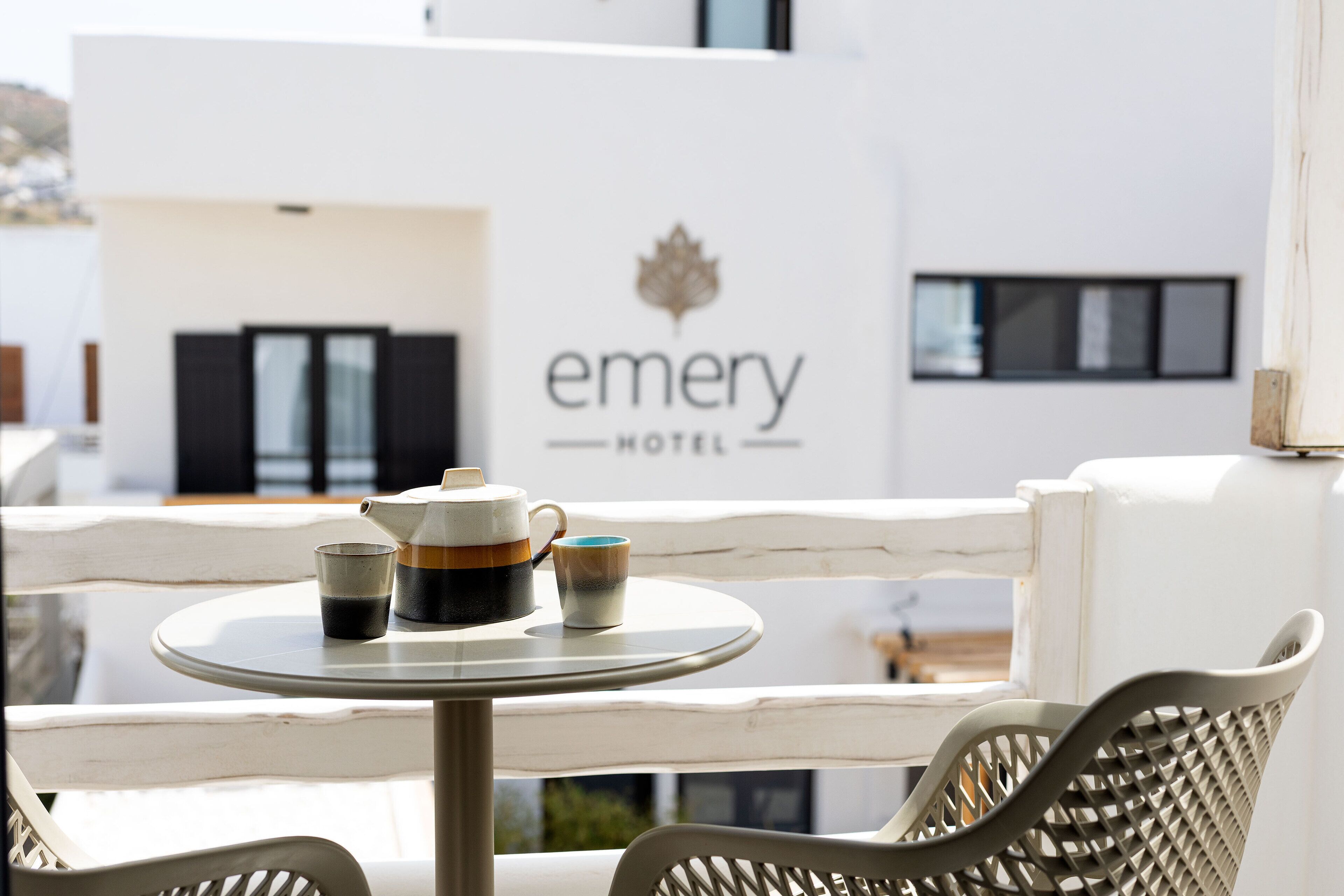 A table with a teapot and cups on a balcony with a view of a hotel sign.