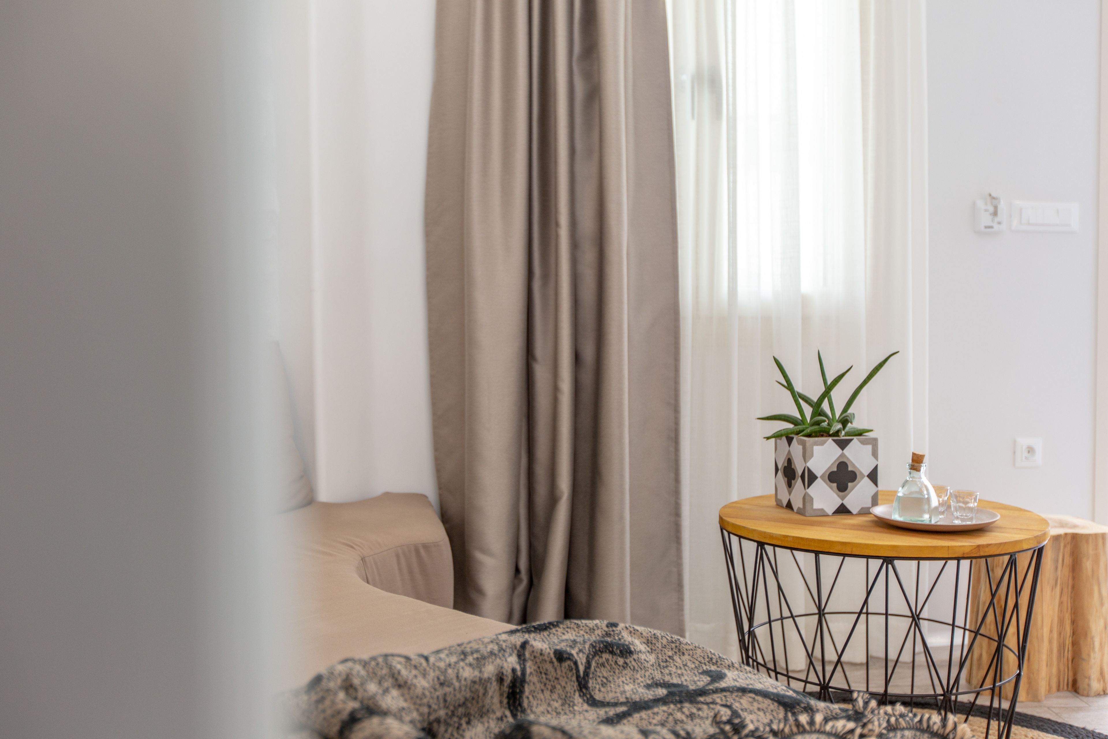 A modern hotel room with a bed, a round wooden table with a potted plant, and a small side table.