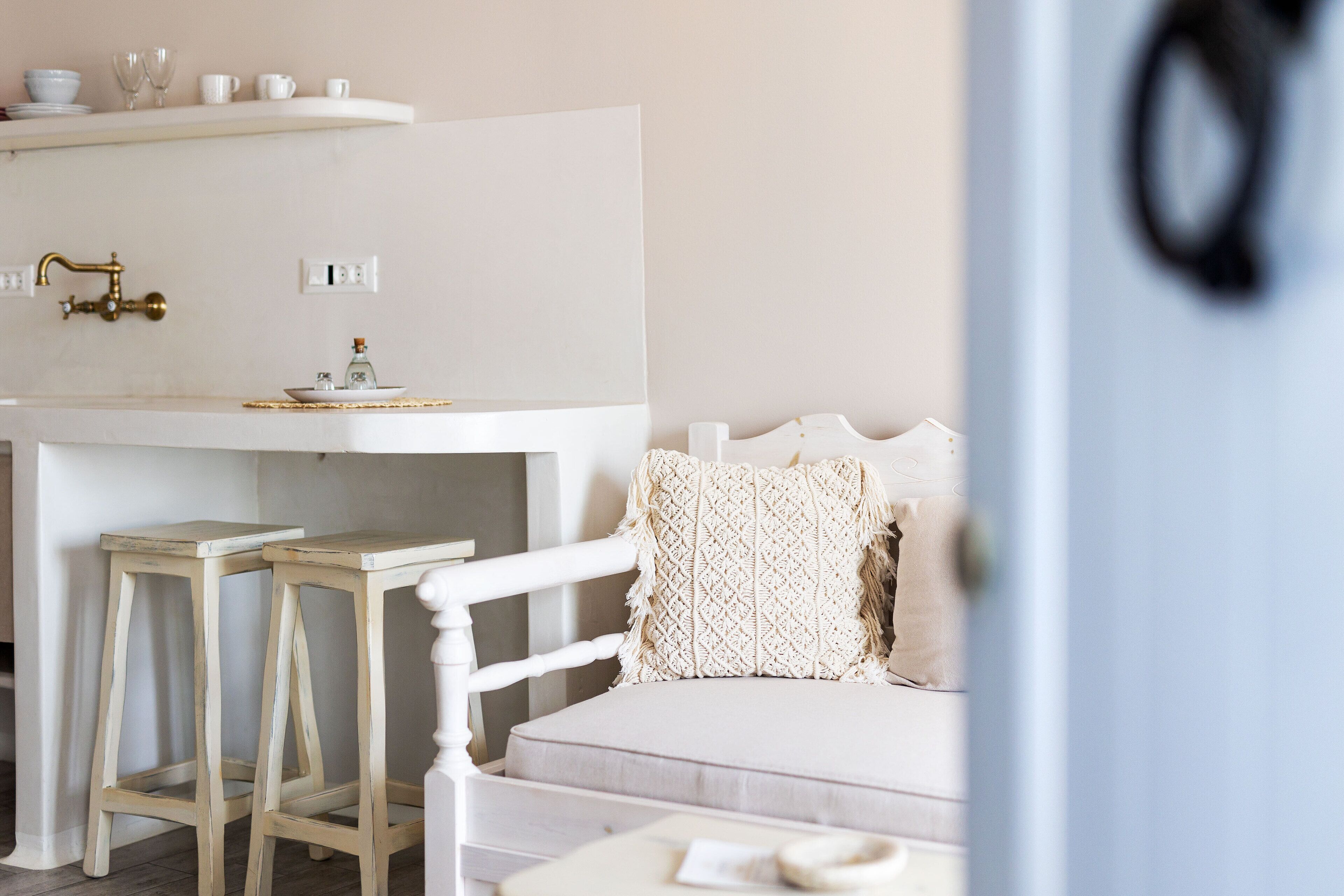 Een wit bed met een gestructureerd kussen, een klein nachtkastje en een witte dressoir met een gouden kraan.