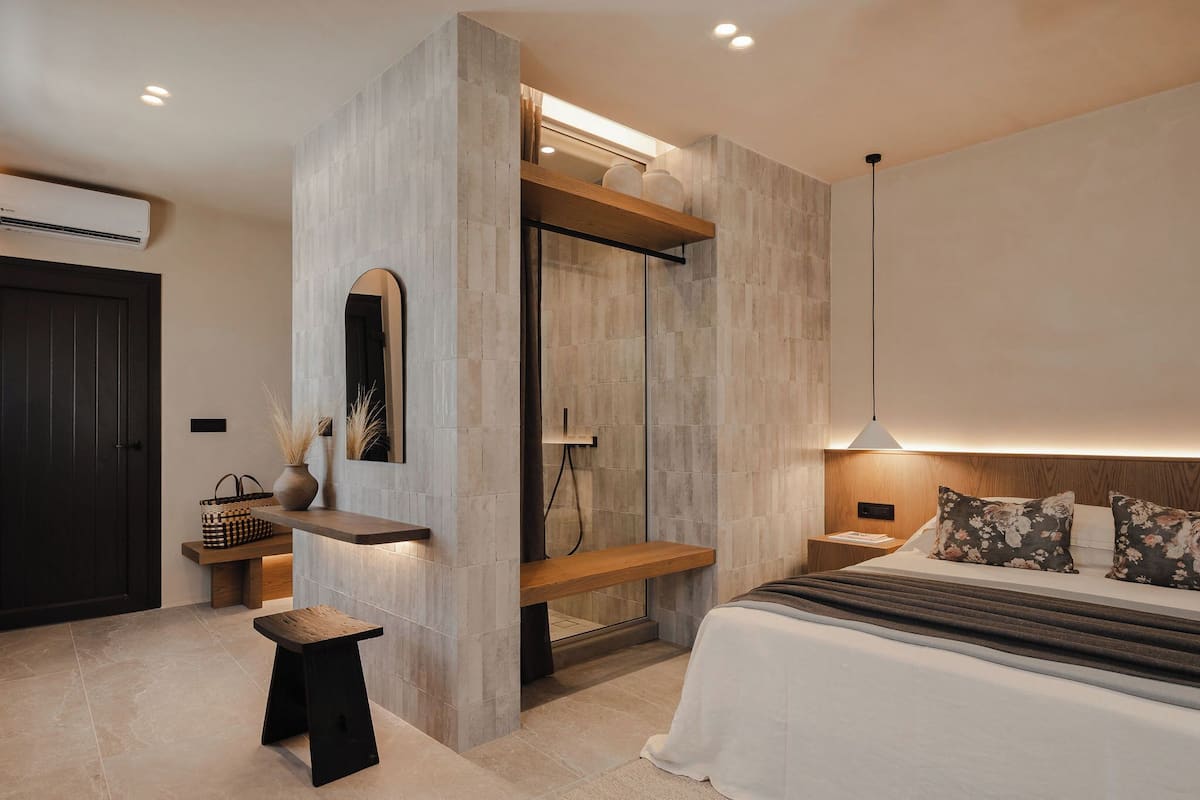 Un dormitorio moderno con una cama grande, un banco de madera, un taburete pequeño y una mesita de noche.