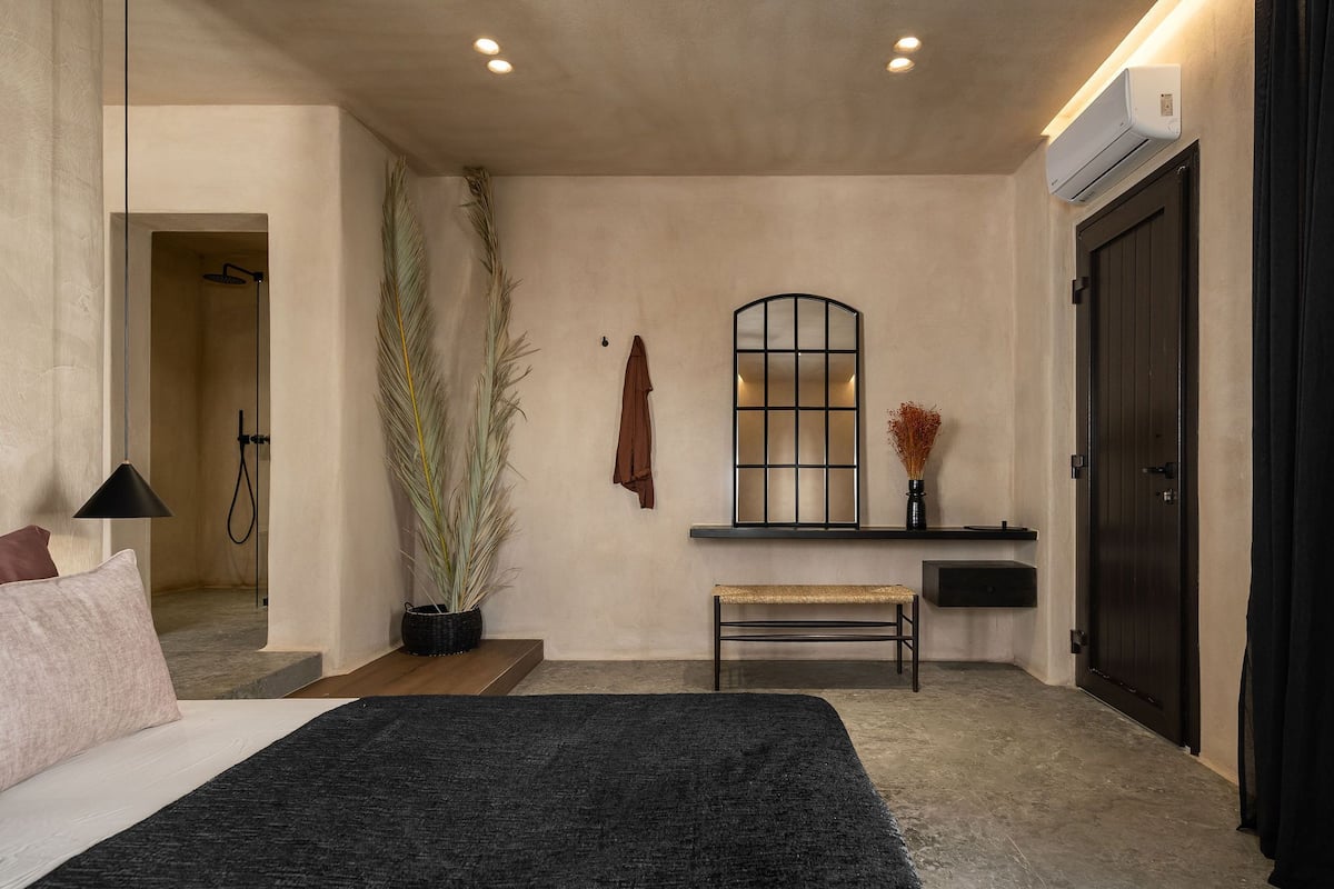 Un dormitorio moderno con una cama grande, un banco, una planta en maceta, una toalla colgada y una ventana con vistas.