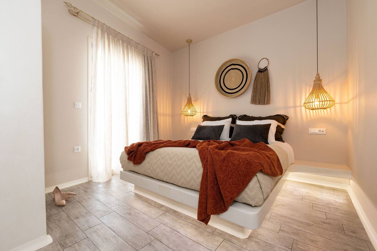 Un dormitorio con cama, cortinas, luces fijadas a la pared y un adorno de pared tejido.