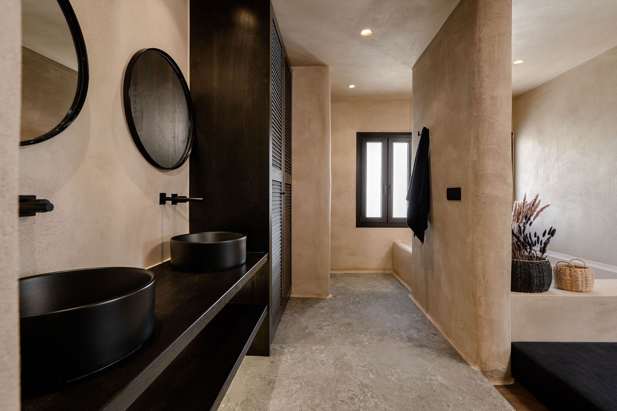 Un baño moderno con un lavabo negro grande, un espejo redondo y un mueble de tocador de madera oscura.