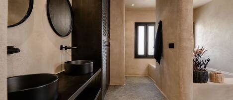 Un baño moderno con un lavabo negro grande, un espejo redondo y un mueble de tocador de madera oscura.