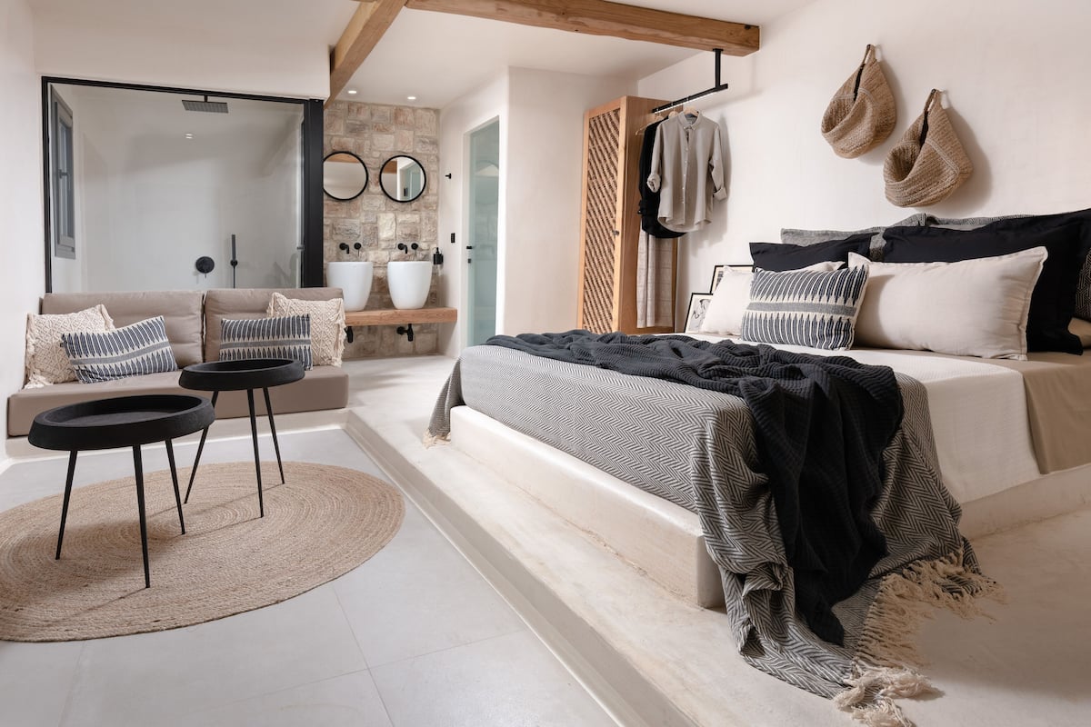 Un dormitorio moderno con una cama grande, un sofá, una mesita y un baño con pared de piedra y un espejo amplio.