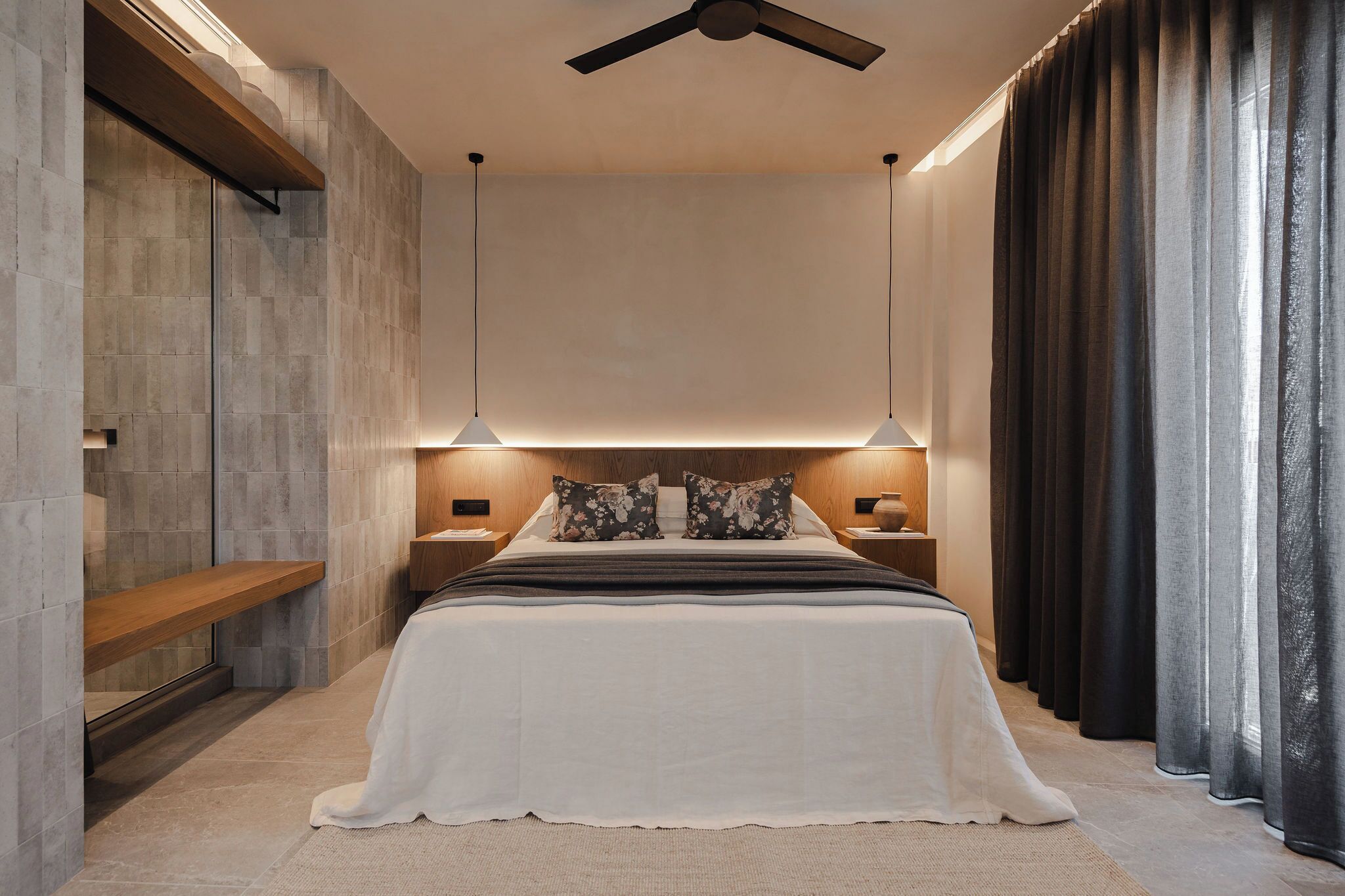 A modern bedroom with a large bed, two bedside tables, a ceiling fan, and a window with dark curtains.