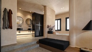 Une salle de bain moderne avec un grand miroir, deux vasques, un banc noir et un vase décoratif.
