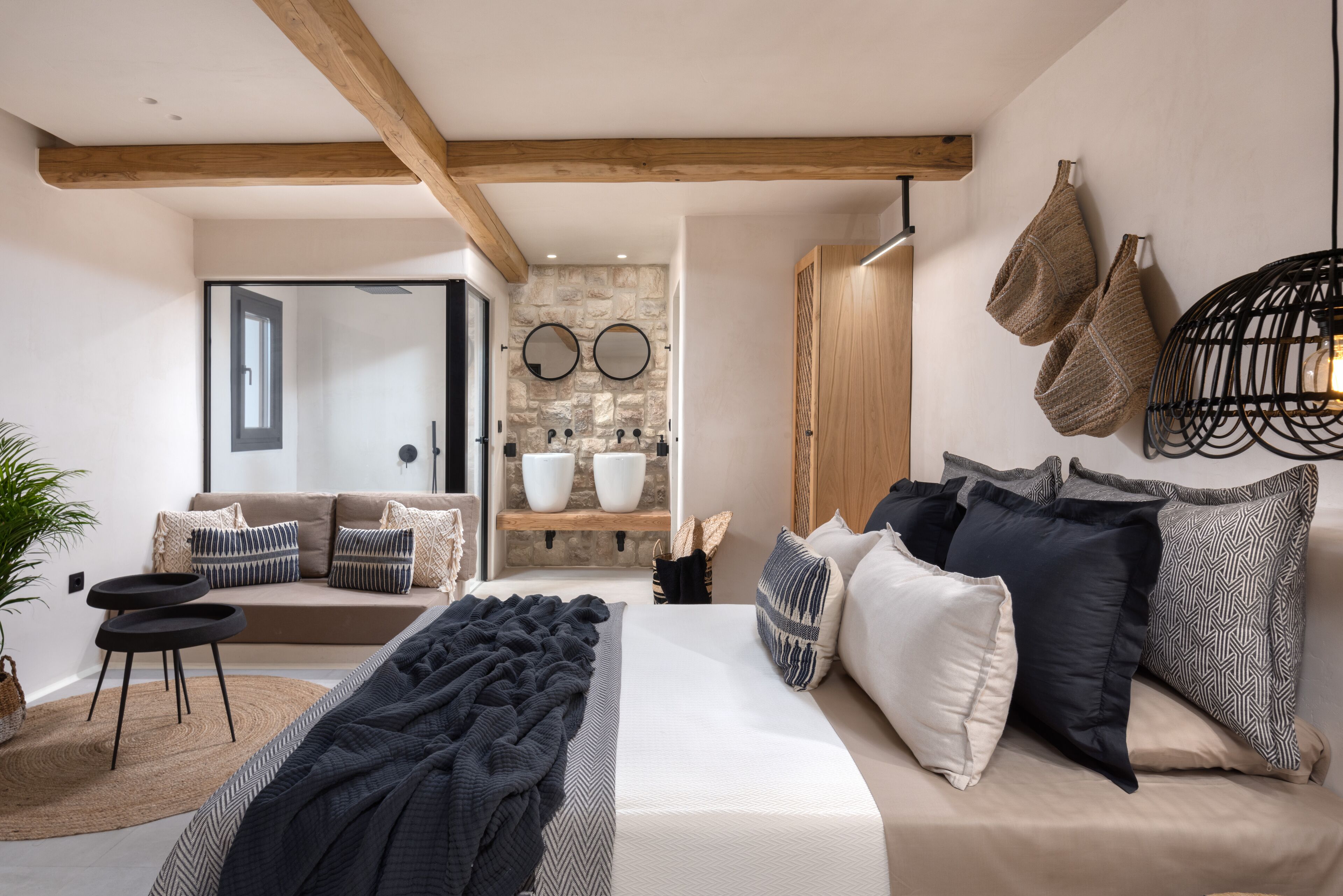 Un dormitorio moderno con una cama grande, un sofá y una pared de piedra con dos espejos.