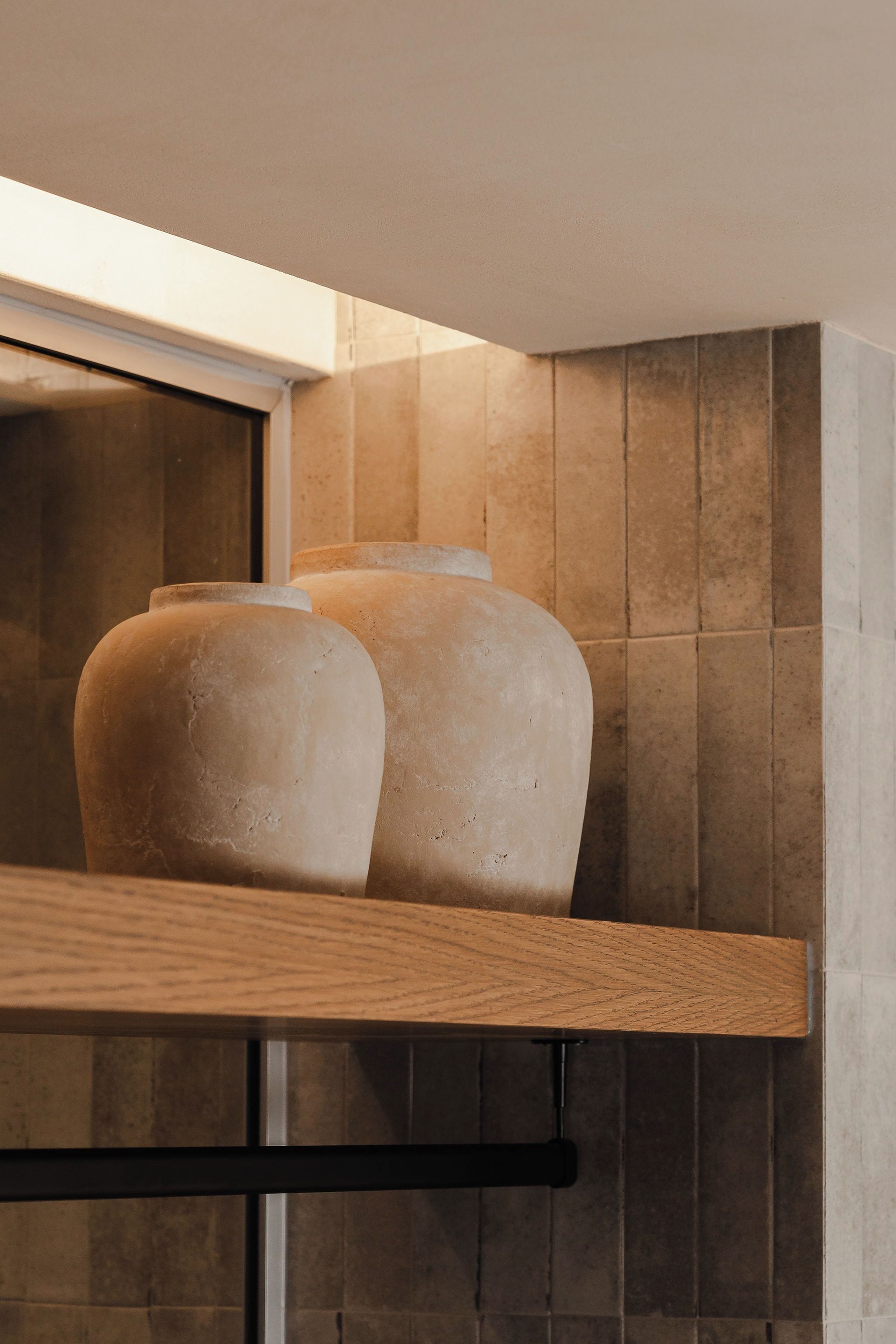 Ein Badezimmer mit einem Holzbodenregal, das zwei Keramikvasen, eine Fliesenwand und ein Fenster mit Jalousien zeigt.