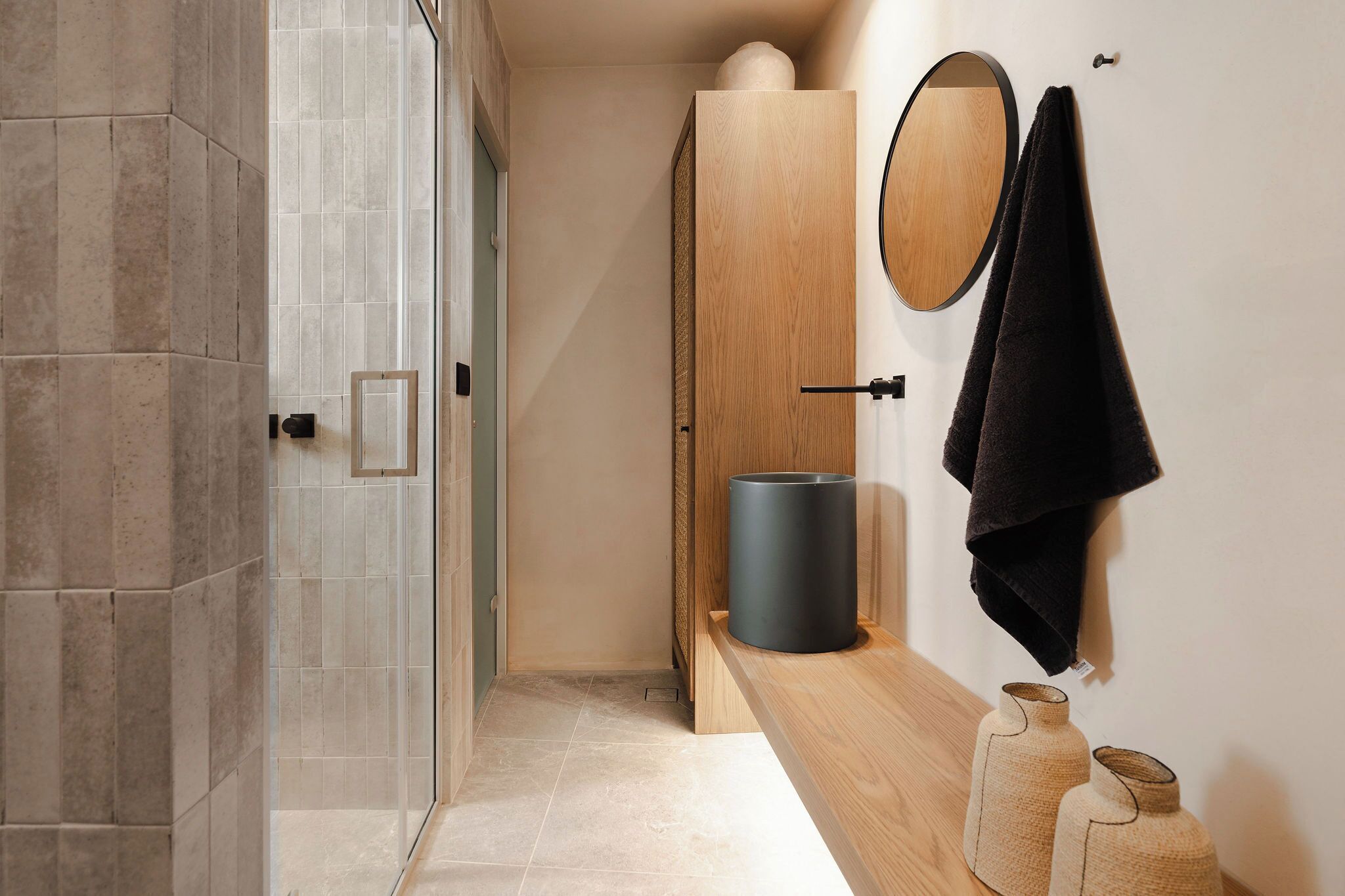 A modern bathroom with a shower, a wooden door, a round mirror, and a towel rack.