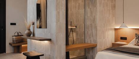 A modern bedroom with a large bed, a wooden bench, a small table, a mirror, and a built-in shower.