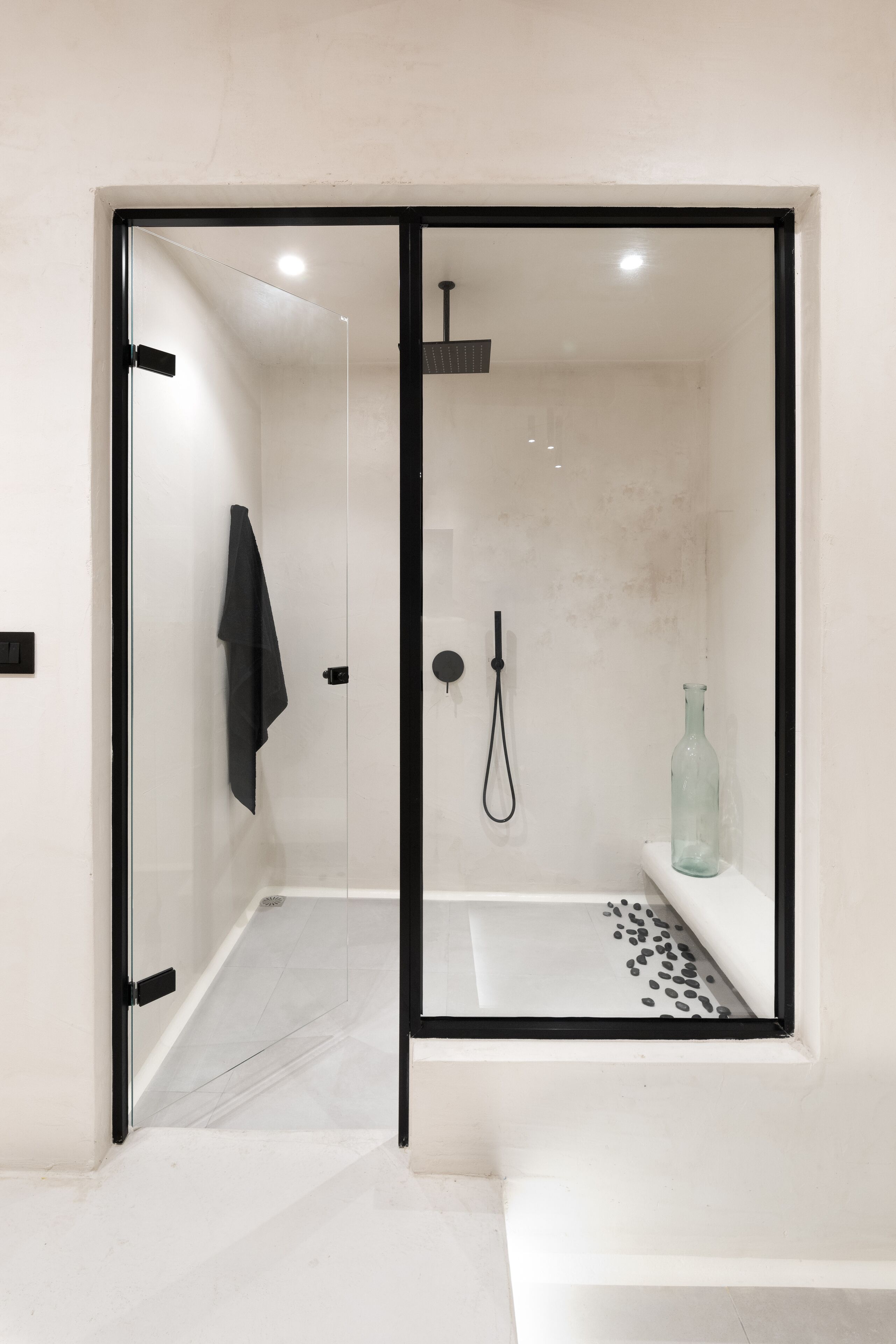 A modern shower area with a glass door, a handheld showerhead, and a shelf with a bottle.