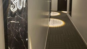 Un couloir orné d’un pilier en marbre sur lequel est inscrit le numéro 307, doté d’un éclairage encastré et recouvert d’une moquette à motifs.