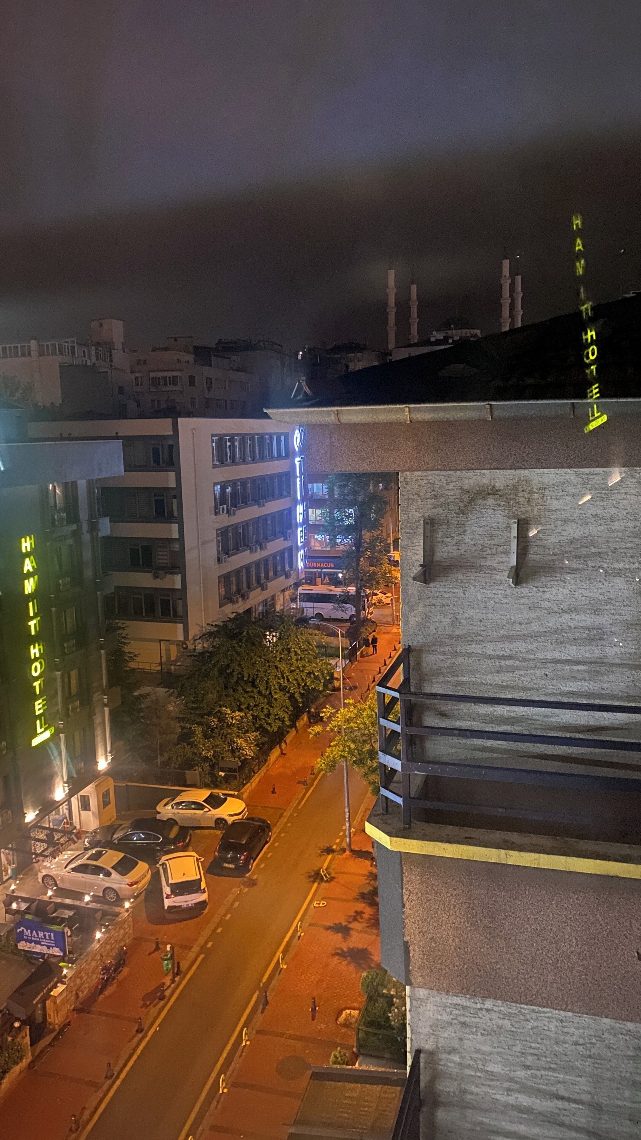 Vista nocturna de una calle con edificios, un autobús y coches estacionados.