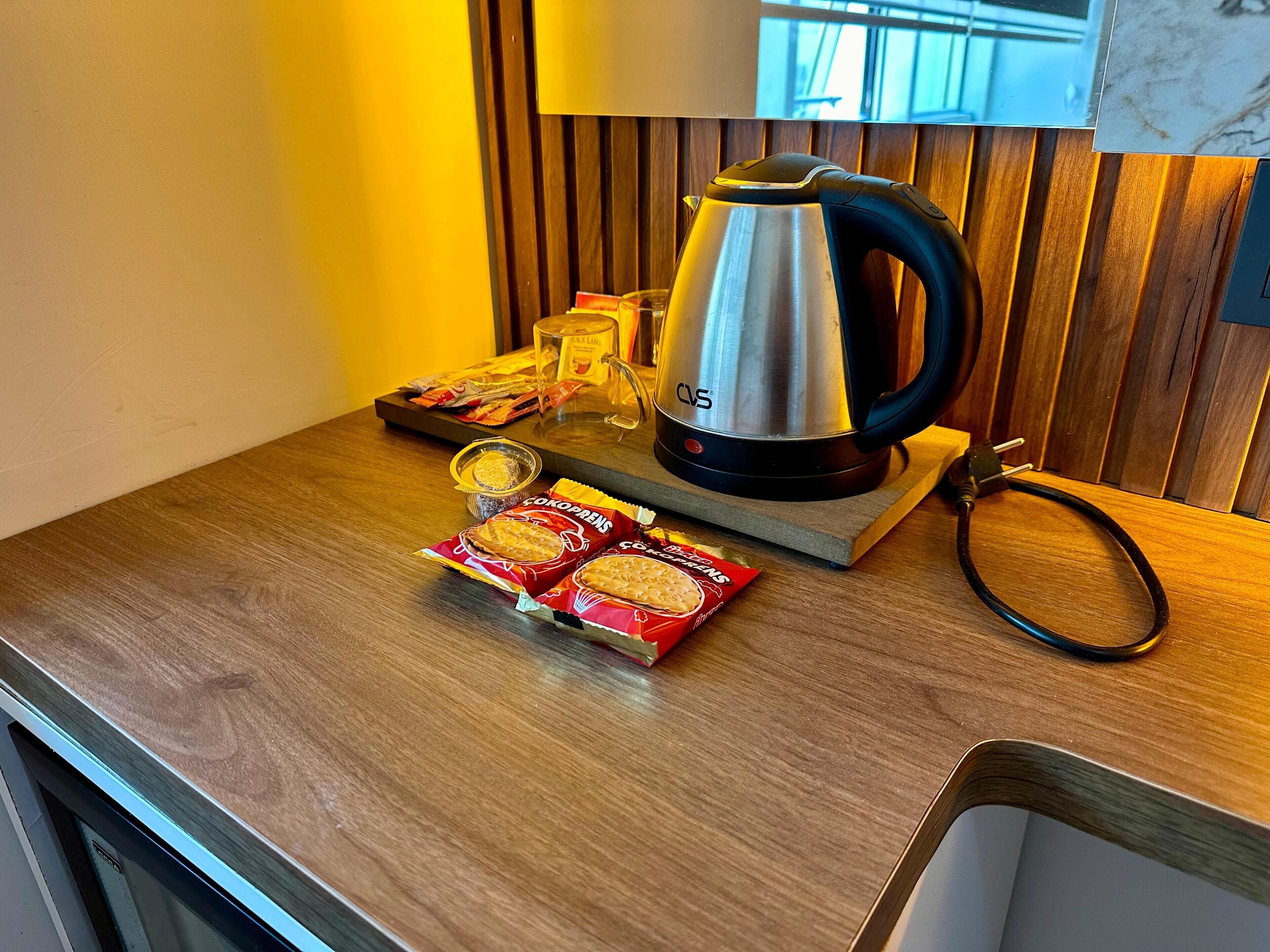 A kitchen counter with a coffee maker, a glass, a packet of biscuits, and a packet of tea.