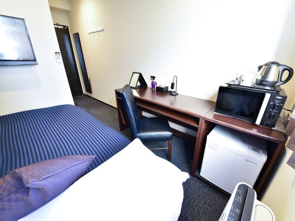 A hotel room with a bed, a desk, a microwave, a coffee maker, and a small refrigerator.