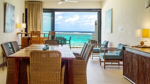 A dining area with a view of the ocean, featuring a wooden table and wicker chairs.
