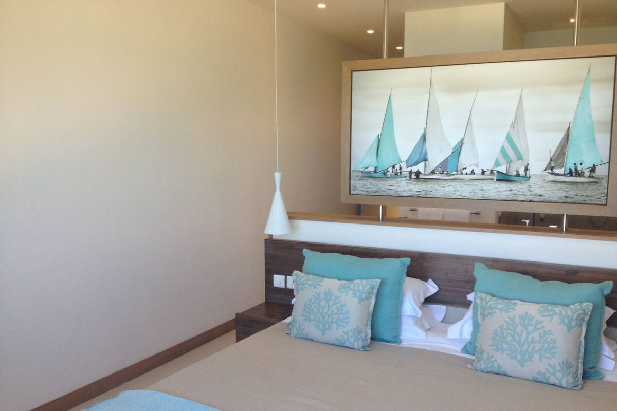 Une chambre à coucher avec un lit, deux oreillers, une table de chevet, un téléviseur fixé au mur et un luminaire au plafond.