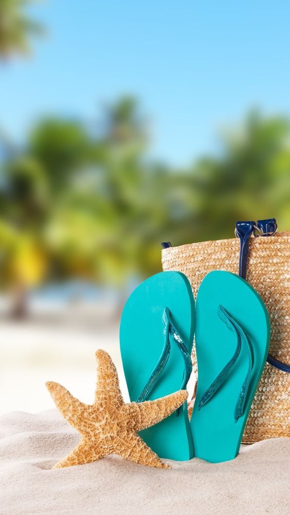 Flip-flops, een zeester en een strooien tas op een zandig oppervlak.