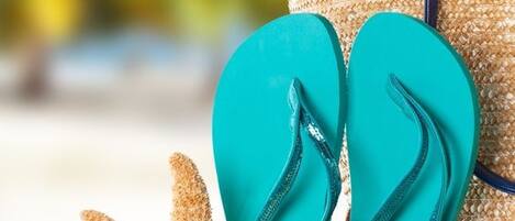 A pair of flip-flops, a starfish, and a straw bag on a sandy surface.