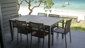 A deck with a table and chairs overlooking a beach with boats.