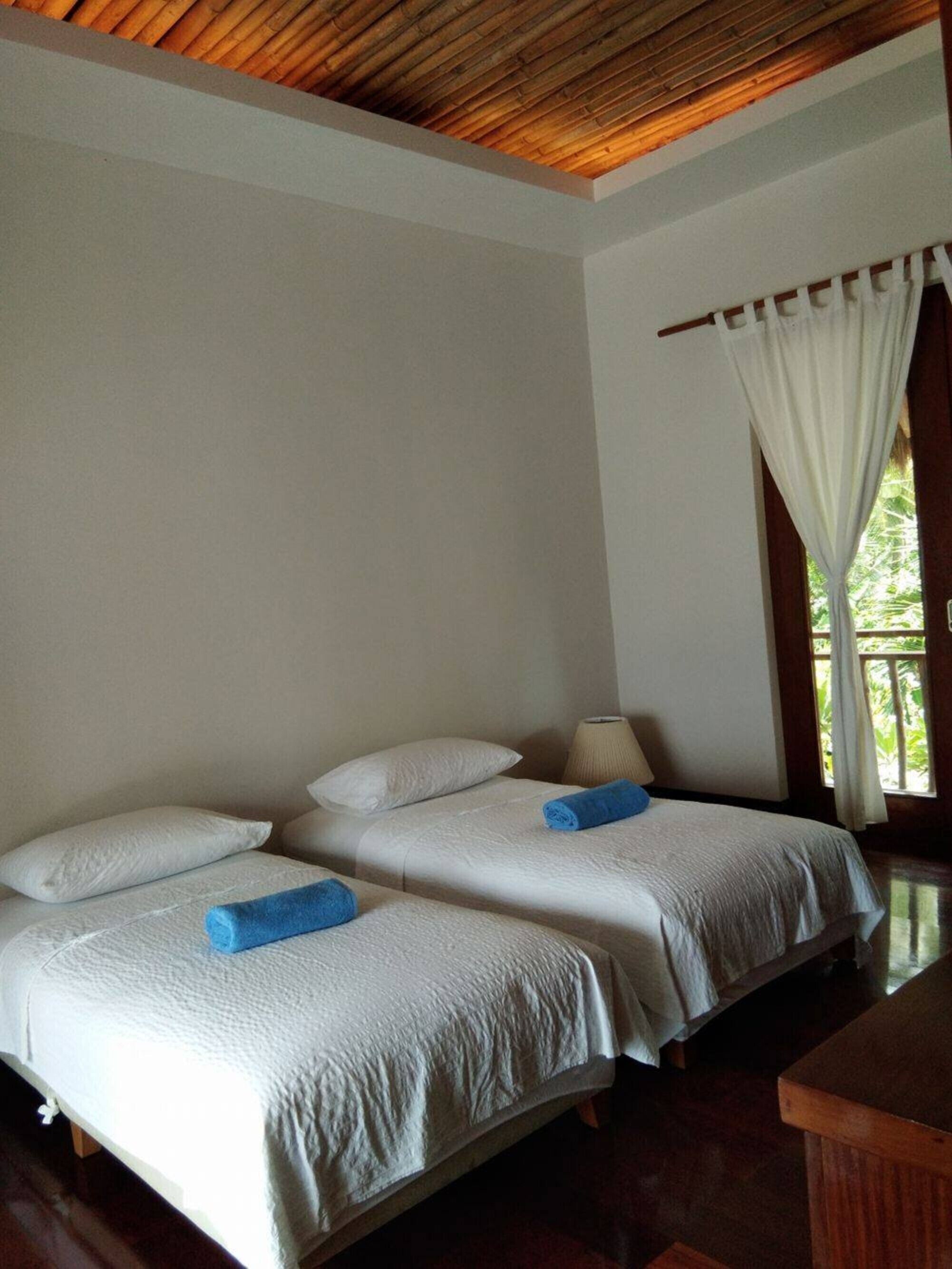 Habitación con dos camas, ropa de cama blanca, techo de madera y ventana con cortinas.