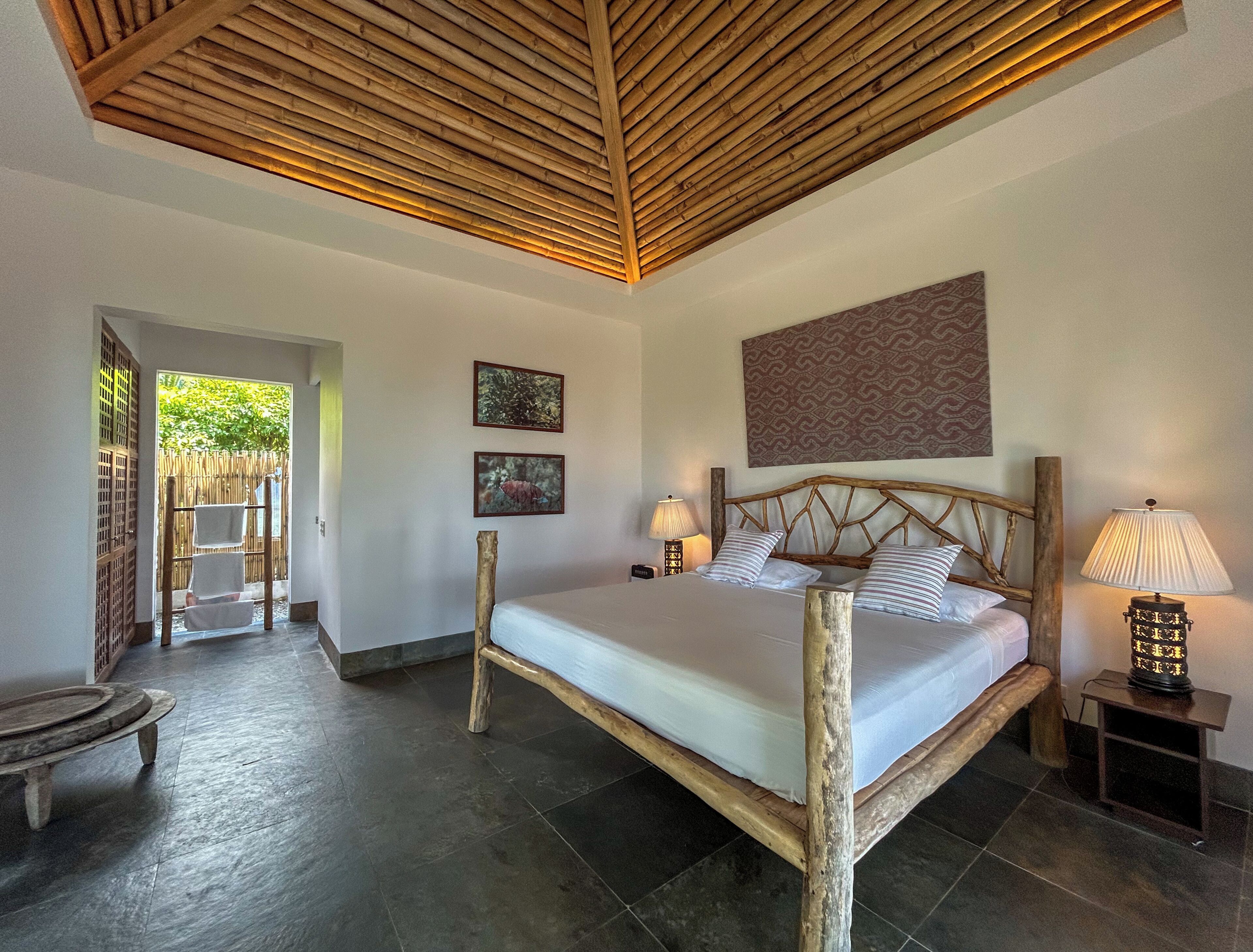 A room with a bed, two wall-mounted lamps, a wooden headboard, and two framed pictures.