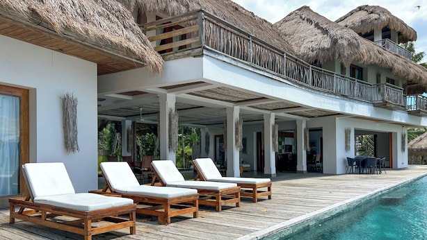 Un complexe hôtelier doté d’une piscine, d’une terrasse en bois, de bâtiments à toits de chaume et de chaises longues.