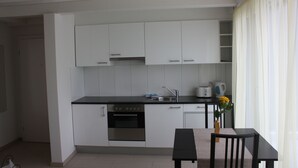 A modern kitchen with white cabinets, a black countertop, a built-in oven, and a sink. There is a small dining table with a bench and a vase with flowers. - Swiss Star Residences (Zürich)