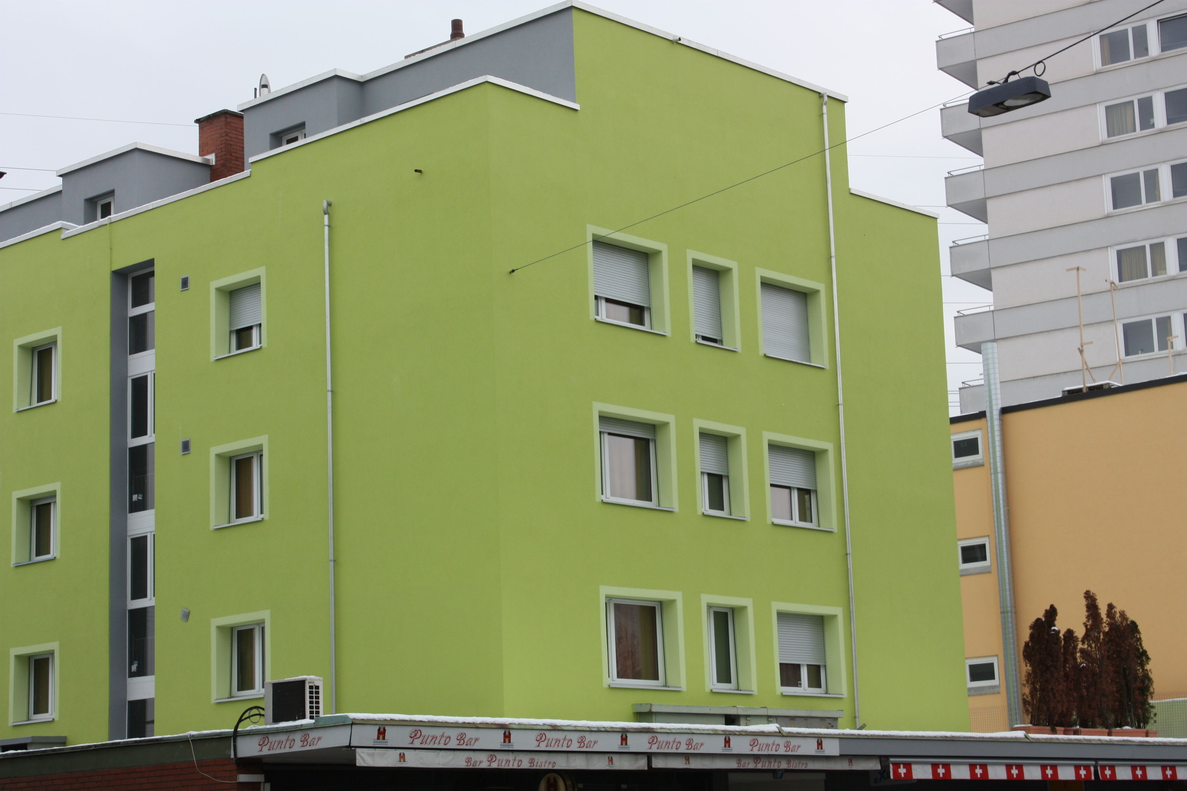 A multi-story building with a green facade, multiple windows, and a flat roof.