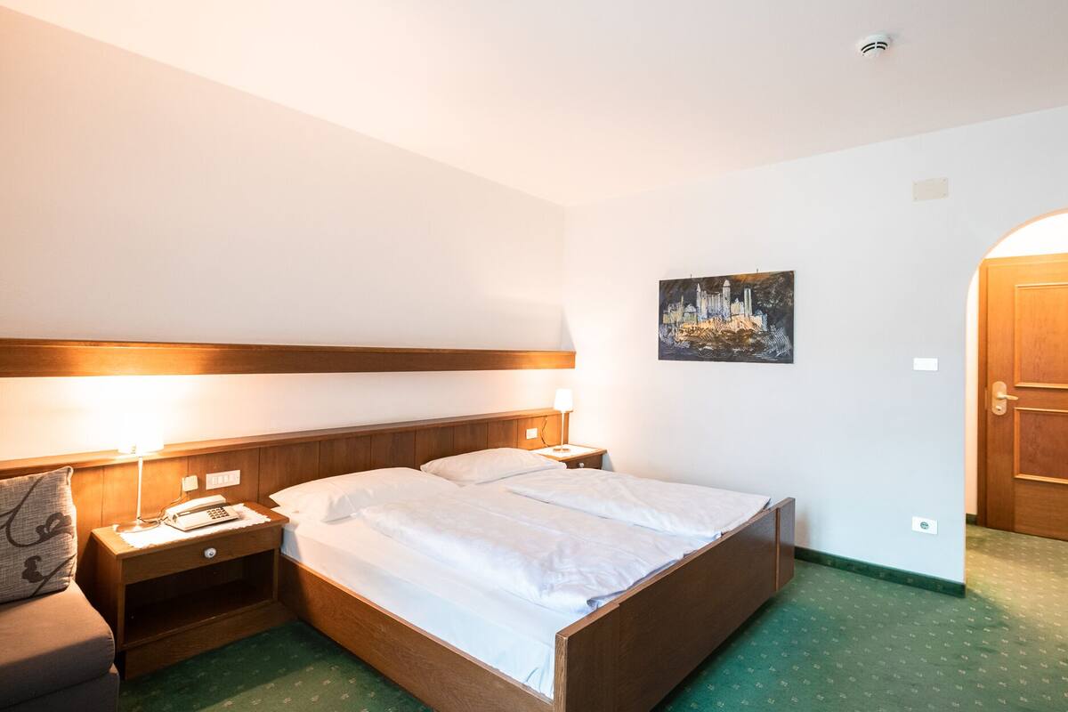 A hotel room with a wooden bed, bedside tables, a lamp, a painting, and a green carpet.