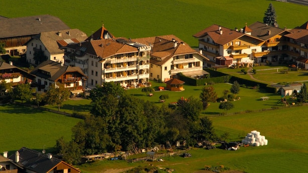 A multi-story hotel with balconies, surrounded by green fields and trees.