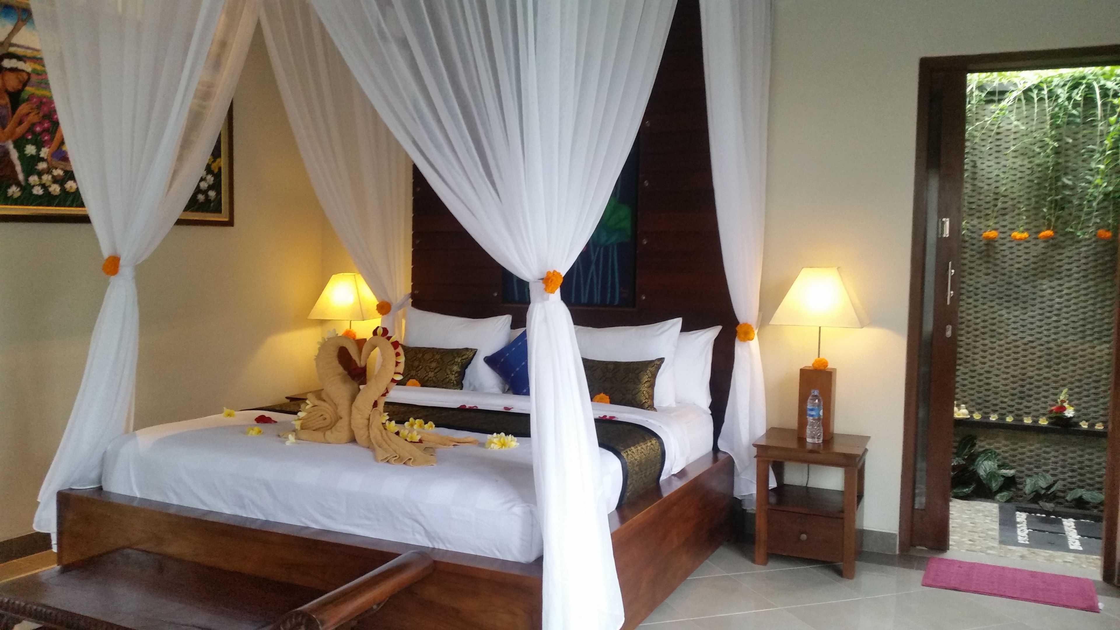A bed with a canopy, two bedside lamps, a water bottle on a nightstand, and a door leading to a garden.