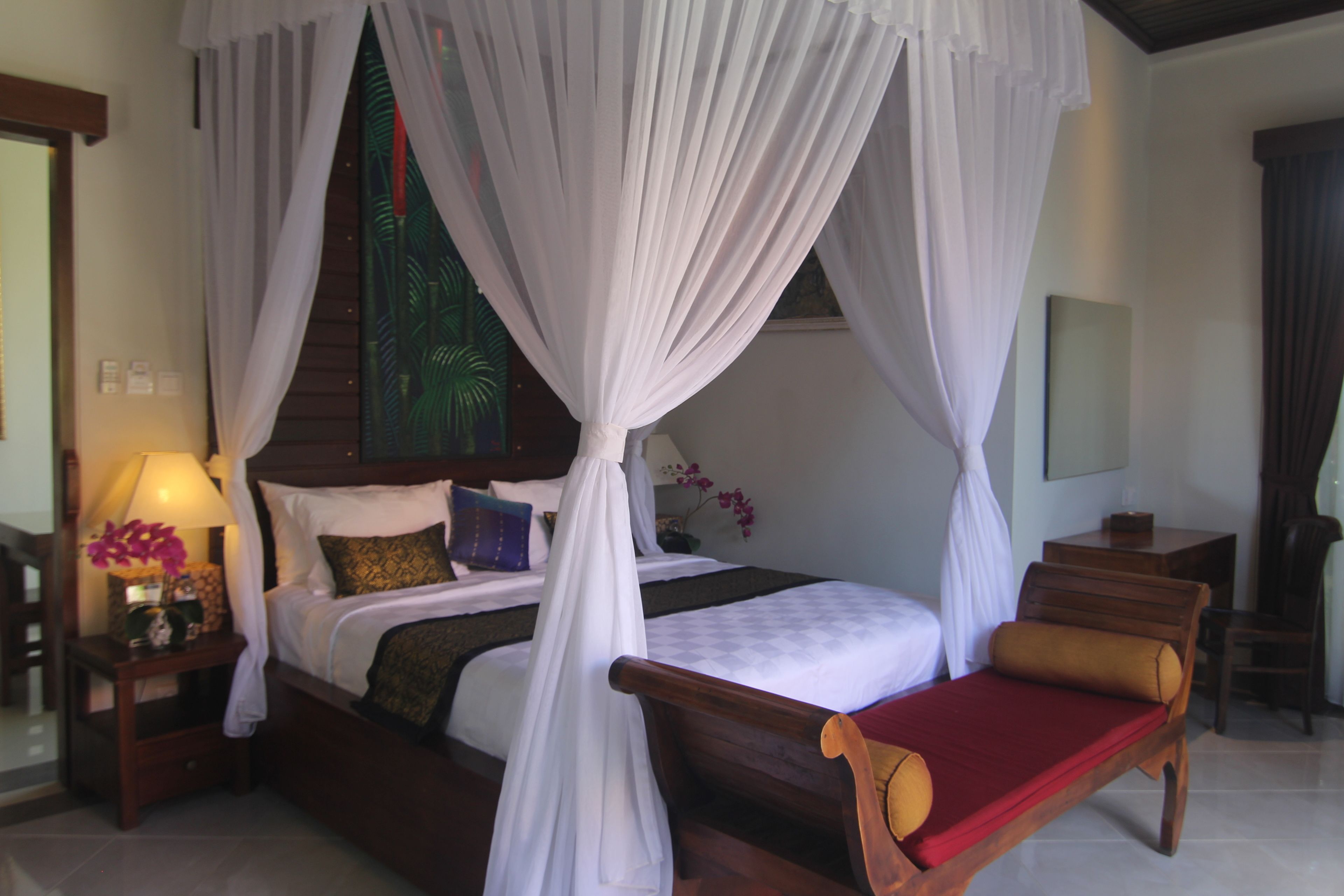 A four-poster canopy bed with a red bedspread and a wooden bench beside it.