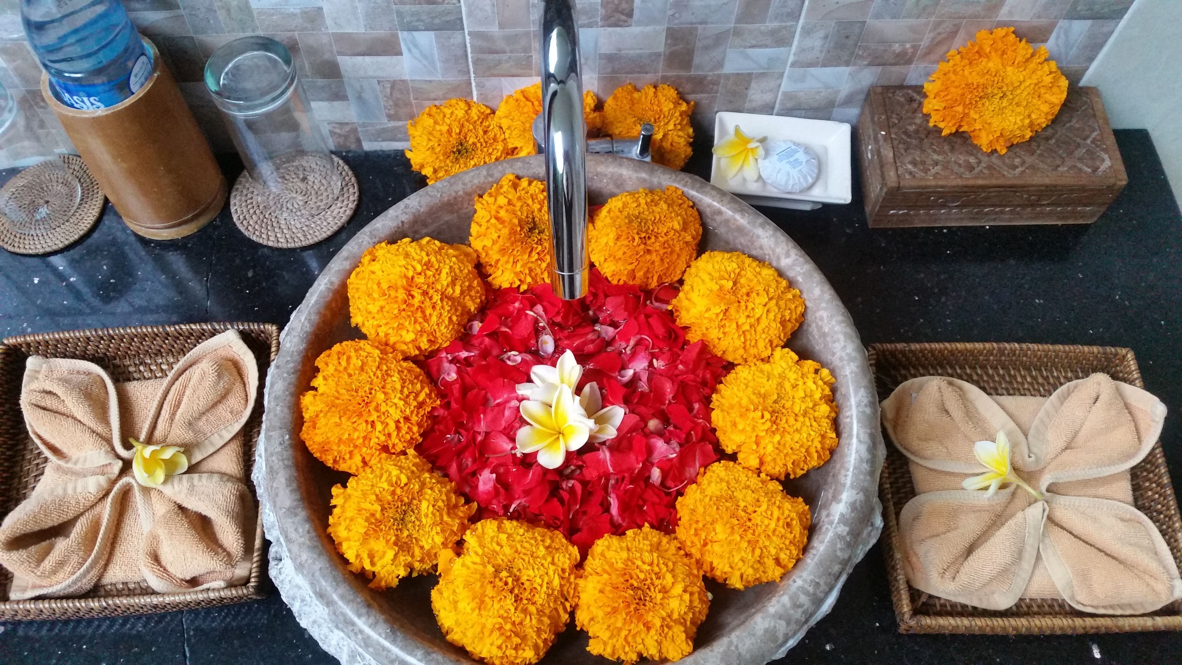 A bathroom sink with a bowl of marigold flowers and rose petals, surrounded by towels and a soap dish.