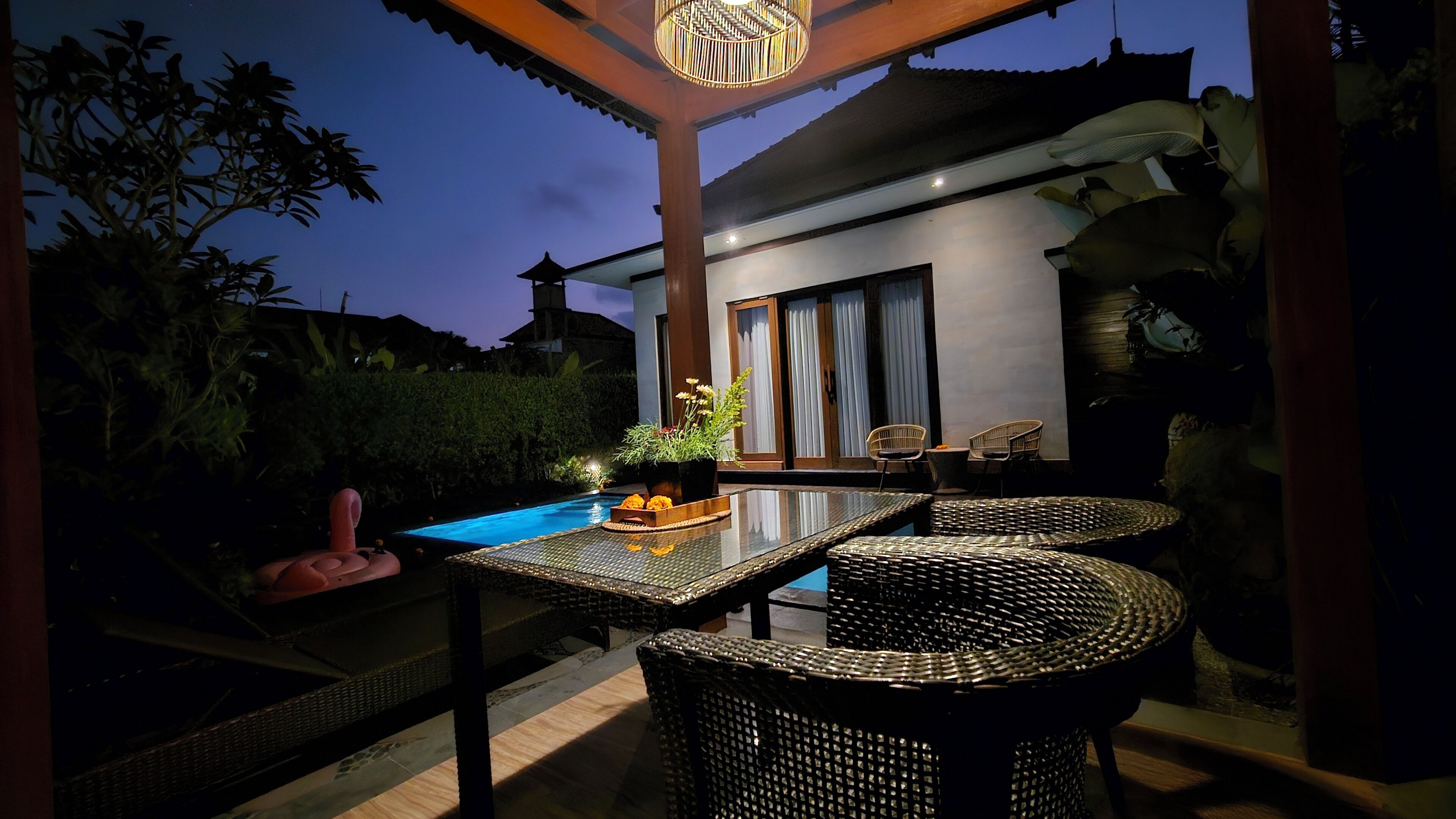 A covered outdoor area with a pool, wicker furniture, and a potted plant.