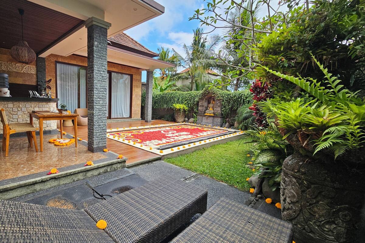 A modern house with a stone exterior, a wooden deck, and a garden with a red floral carpet.