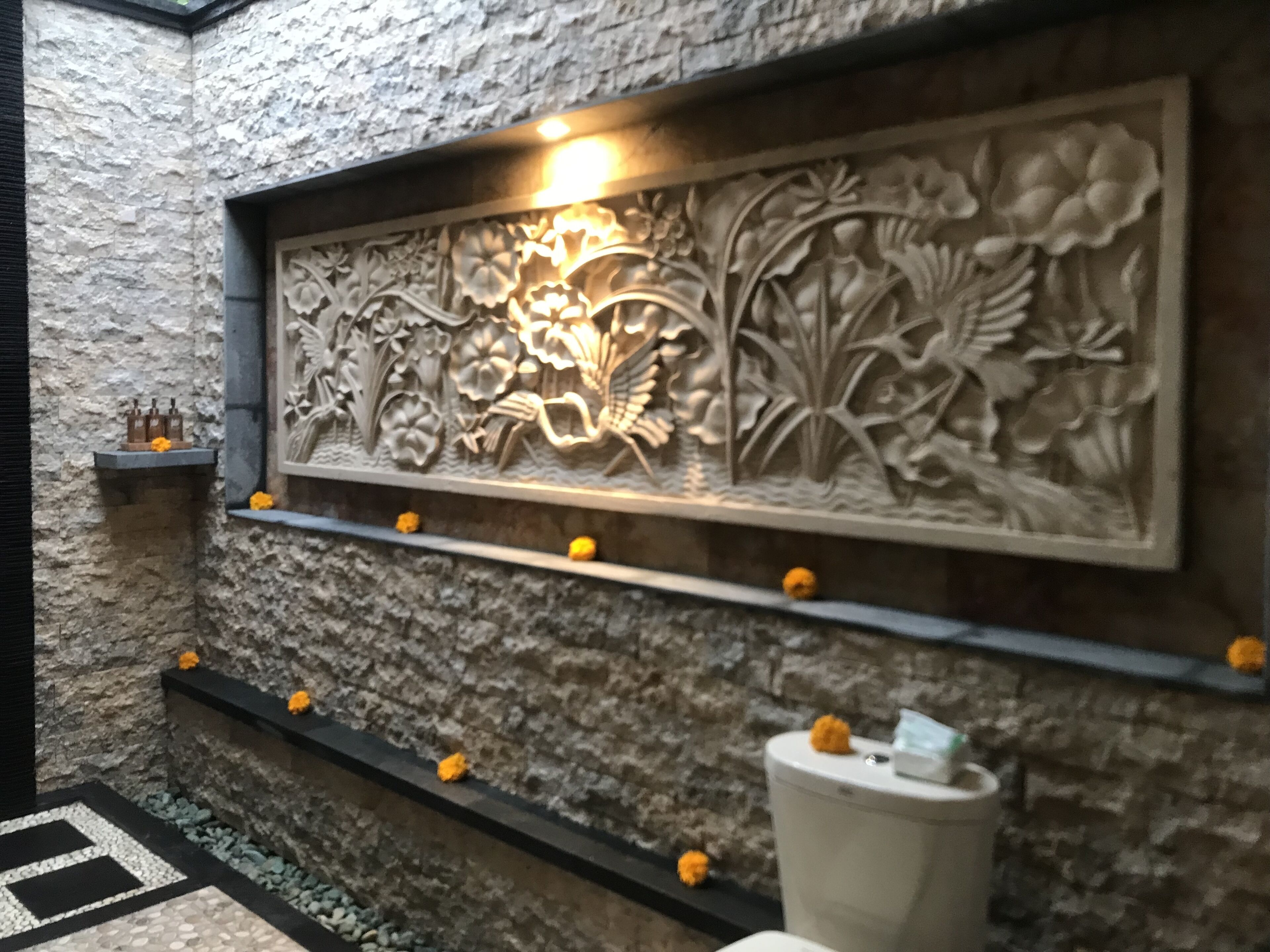 Een stenen muur met een bloemenreliëf en een plank met flessen en bloemen.