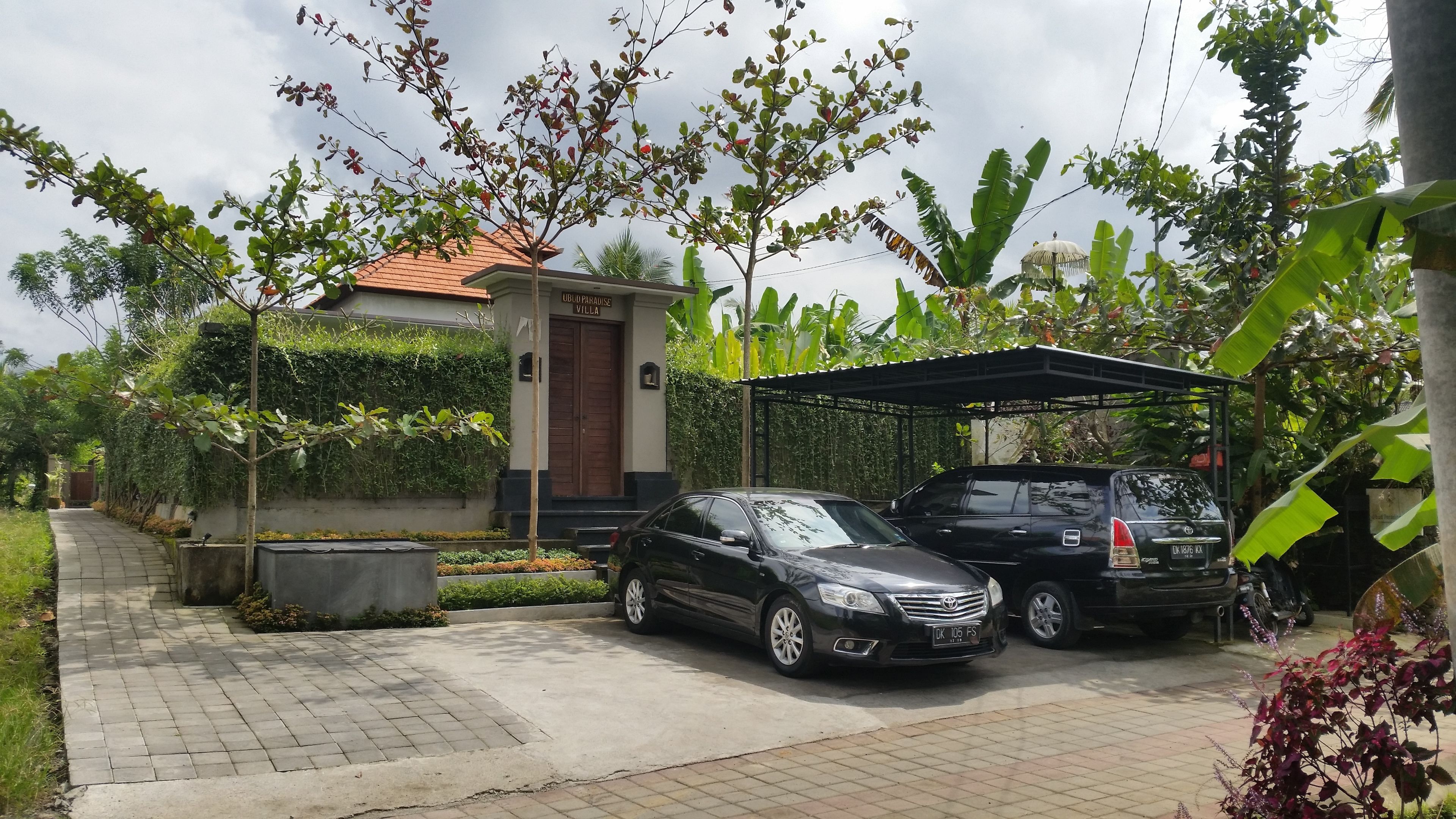A black car parked in front of a building with a tiled roof and a covered parking area.